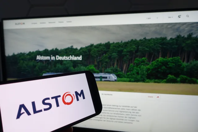 Smartphone mit dem Logo Alstom vor einem Bildschirm
