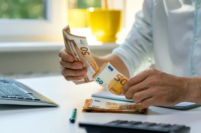 Ein Mann zählt 50-Euro-Scheine vor einem Computer.