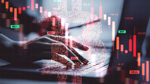 Ein roter Bitcoin-Kurs, dahinter arbeitet jemand an einem Laptop.