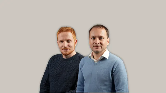 Auf dem Bild sind zwei Männer vor neutralem Hintergrund zu sehen: Links steht Georg Buschmann und rechts Henry Philippson. Beide blicken direkt in die Kamera.