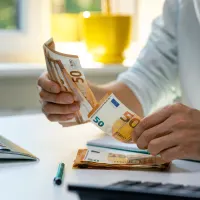 Ein Mann zählt 50-Euro-Scheine vor einem Computer.