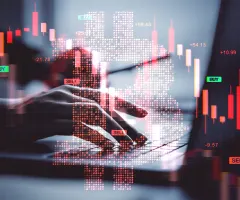 Ein roter Bitcoin-Kurs, dahinter arbeitet jemand an einem Laptop.