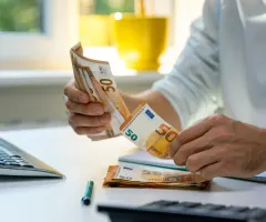 Ein Mann zählt 50-Euro-Scheine vor einem Computer.