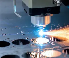 Eine Laserschneidanlage bearbeitet ein Metallblech, während beim Schneidvorgang helle Funken entstehen.
