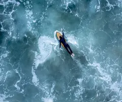 Ein Surfer paddelt auf seinem Surfbrett liegend durchs Wasser